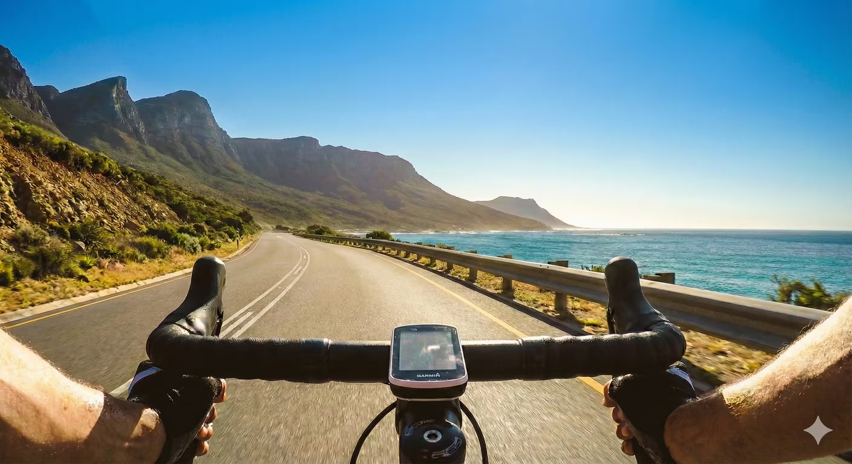 Person riding a bicycle on a scenic road with mountains and ocean view