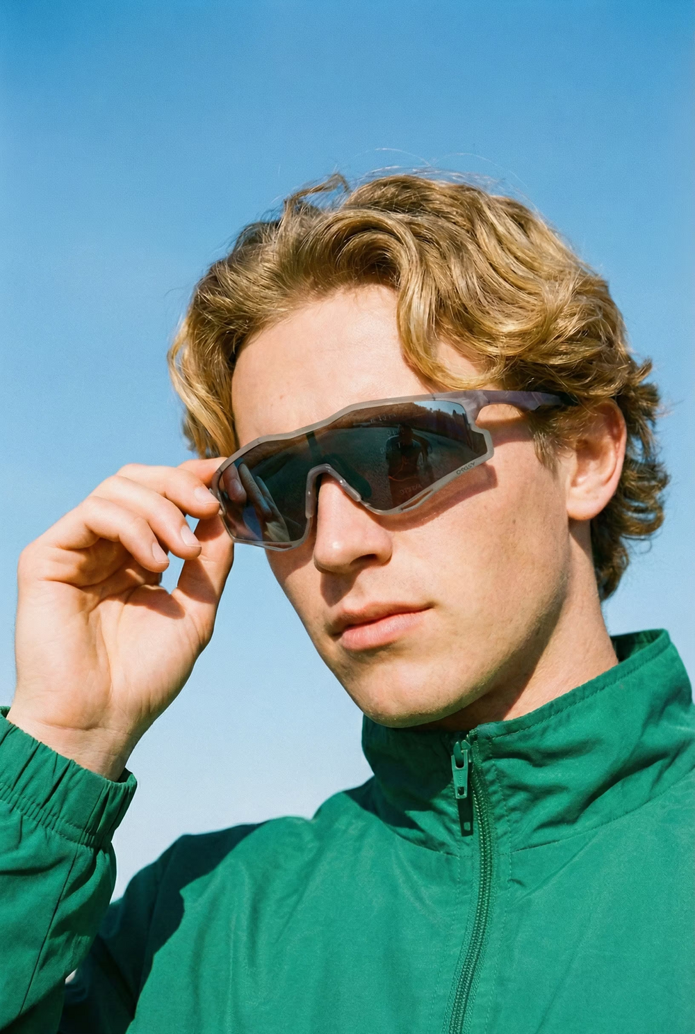 Man wearing sunglasses and a green jacket against a clear blue sky