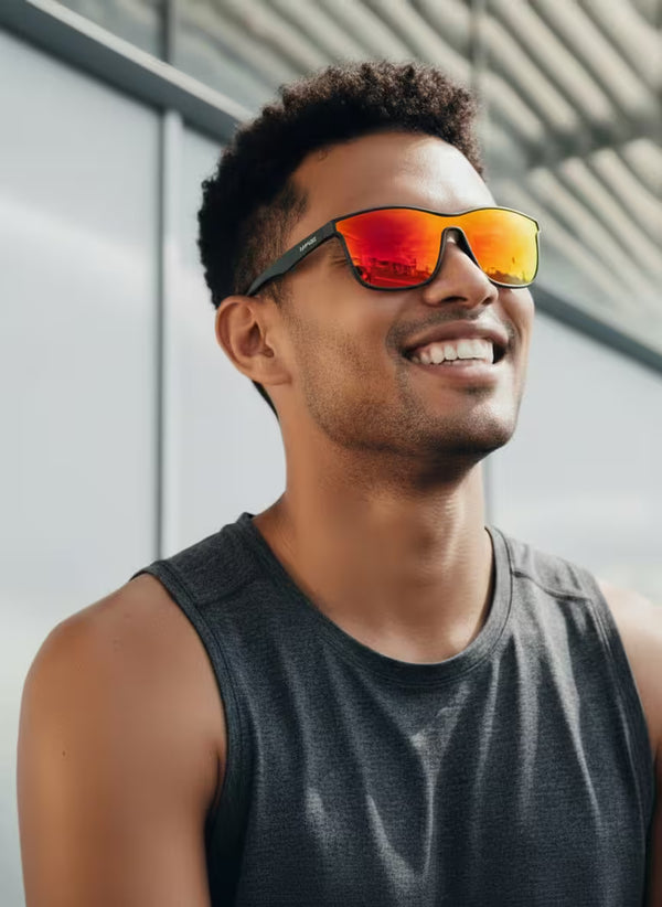 Man wearing sunglasses with a reflective orange lens, smiling outdoors.